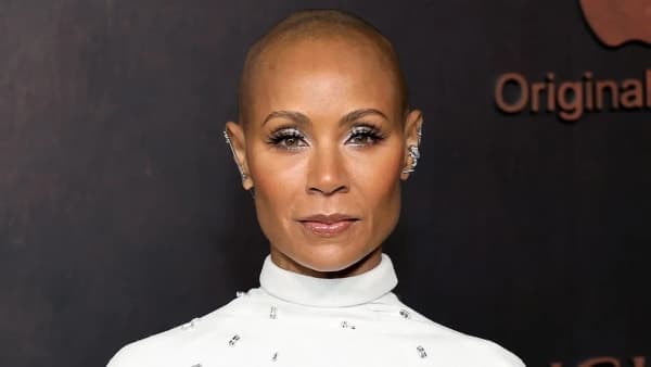 A woman in a formal outfit against a red carpet backdrop