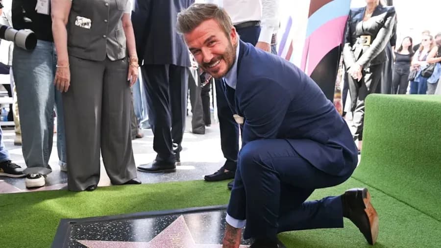 David Beckham smiling at his Hollywood Walk of Fame star ceremony, surrounded by family and friends including Tom Cruise, with a green football-themed carpet visible