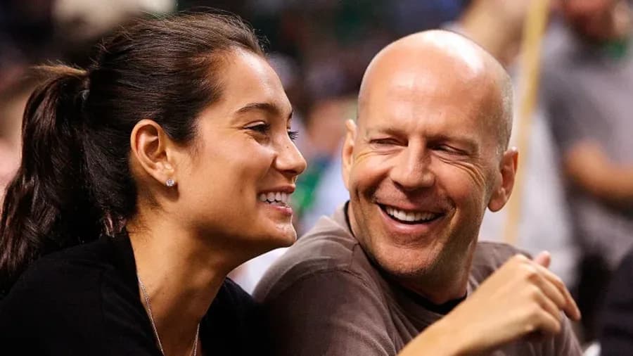 Emma Heming Willis wearing a birthday party hat alongside Bruce Willis, both smiling during a birthday celebration at home