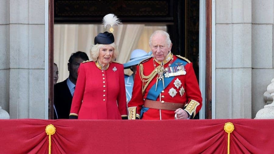 A man in a formal suit and a woman in an elegant outfit walking together on an official engagement, smiling and greeting a crowd
