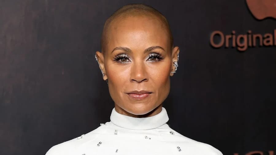 A woman in a formal outfit against a red carpet backdrop